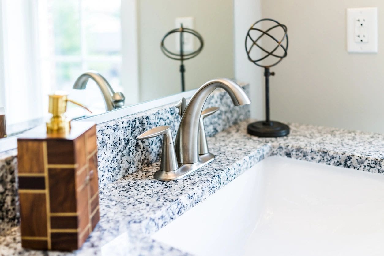 A bathroom sink with marble counter tops and silver fixtures.